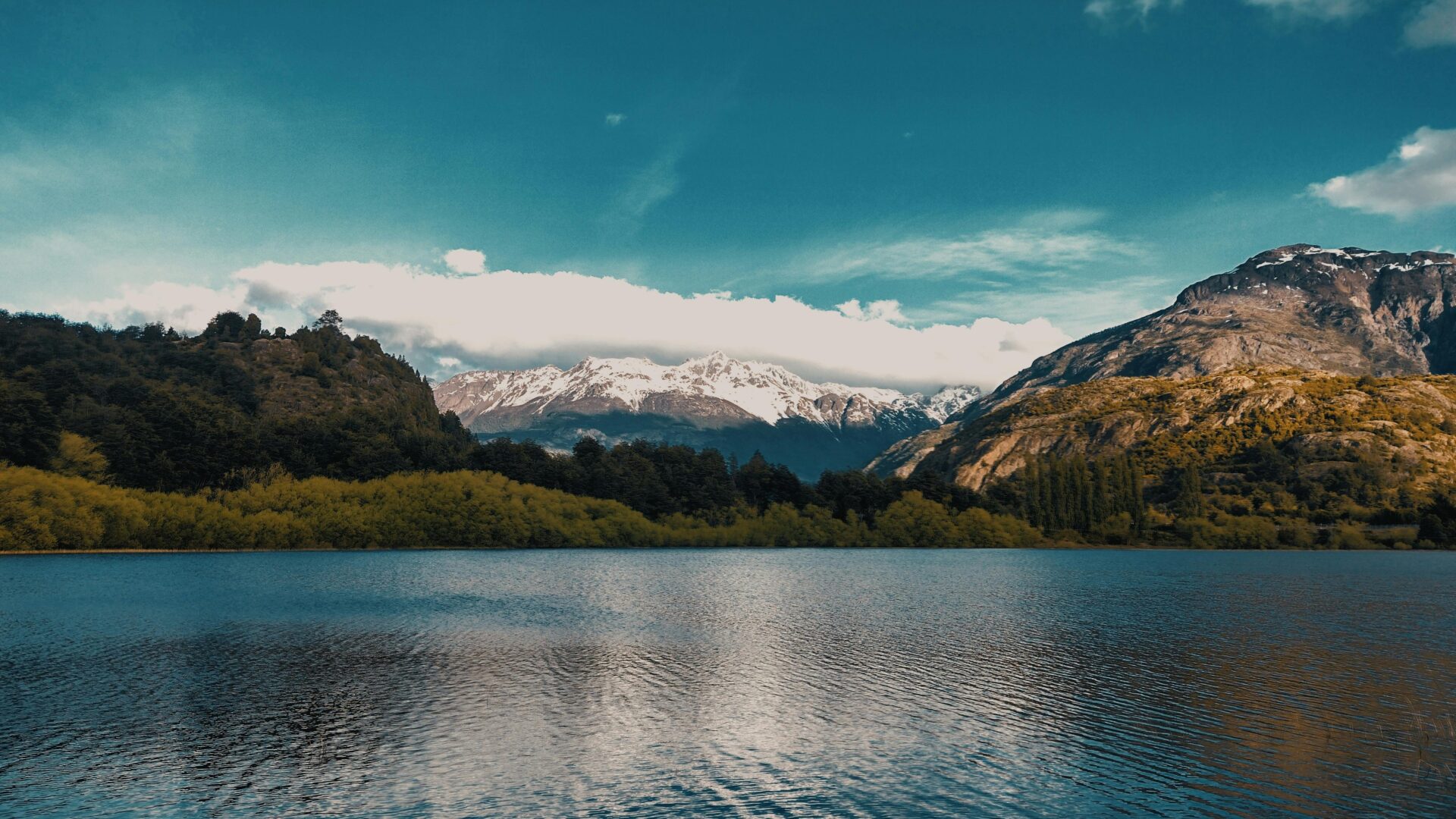 Calm lake with snow-capped mountains and lush greenery in Futaleufú, Chile.